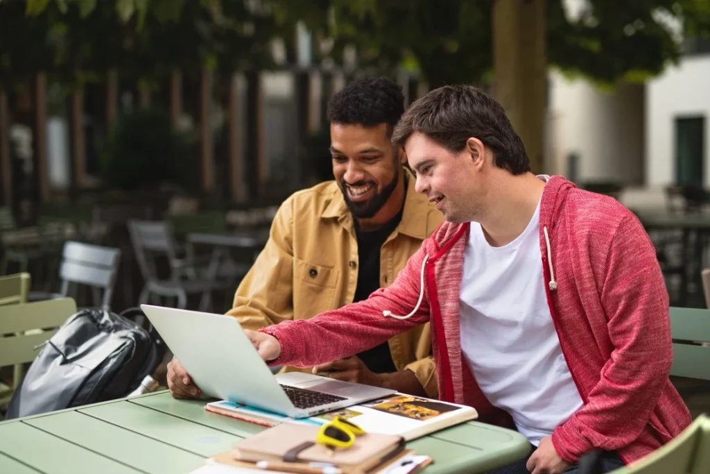 Disabled man with down syndrome looking at laptop with support worker
